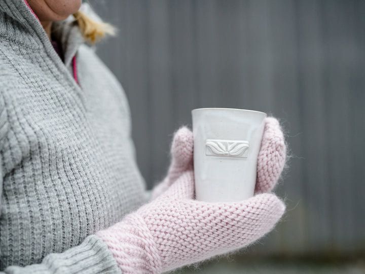Vit keramisk kopp i händer med stickade vantar